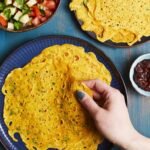 Aranyos, fűszeres palacsinták képe, kézzel tartva, köretként saláta és chutney.