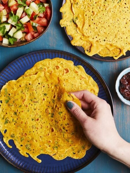Aranyos, fűszeres palacsinták képe, kézzel tartva, köretként saláta és chutney.