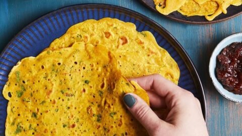 Aranyos, fűszeres palacsinták képe, kézzel tartva, köretként saláta és chutney.