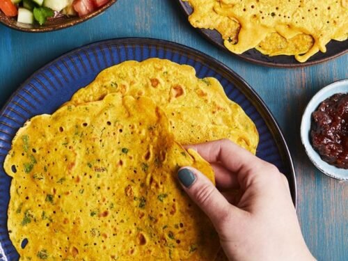 Aranyos, fűszeres palacsinták képe, kézzel tartva, köretként saláta és chutney.