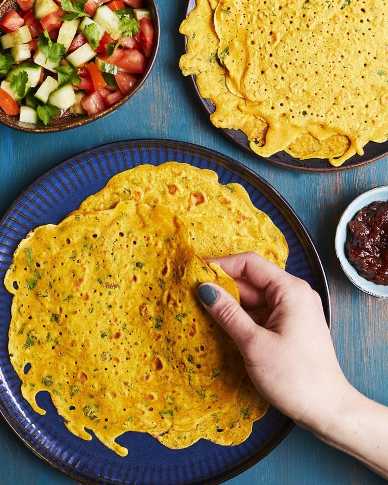 Aranyos, fűszeres palacsinták képe, kézzel tartva, köretként saláta és chutney.