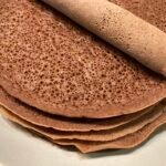 Sült injera palacsinták egy tányéron, egy tekercs injera látható a tetején.