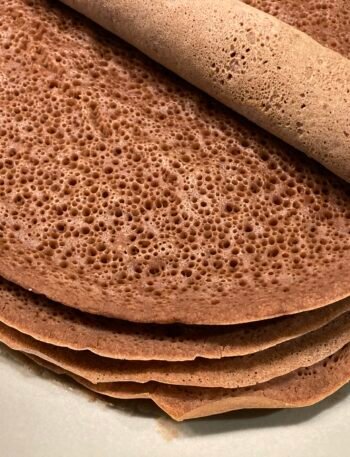 Sült injera palacsinták egy tányéron, egy tekercs injera látható a tetején.