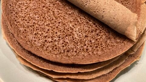 Sült injera palacsinták egy tányéron, egy tekercs injera látható a tetején.
