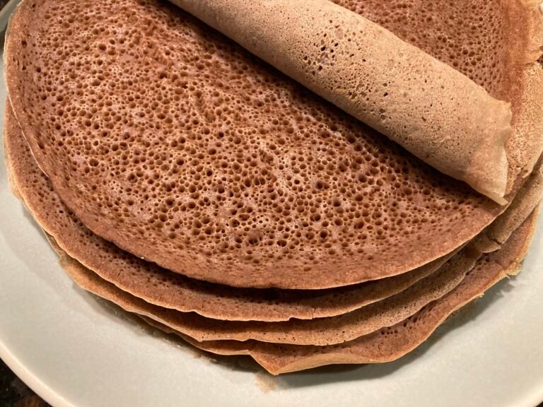 Sült injera palacsinták egy tányéron, egy tekercs injera látható a tetején.