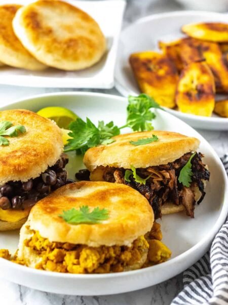 Három arepa különböző töltelékekkel: fekete bab, húsgulyás és tojásos. Korianderrel díszítve.