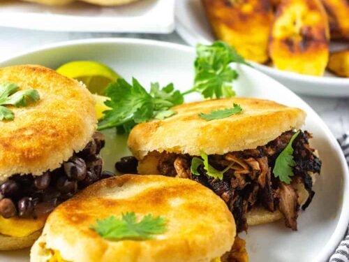 Három arepa különböző töltelékekkel: fekete bab, húsgulyás és tojásos. Korianderrel díszítve.