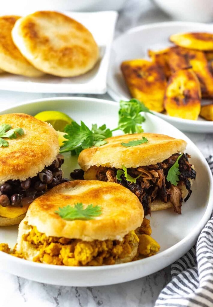 Három arepa különböző töltelékekkel: fekete bab, húsgulyás és tojásos. Korianderrel díszítve.